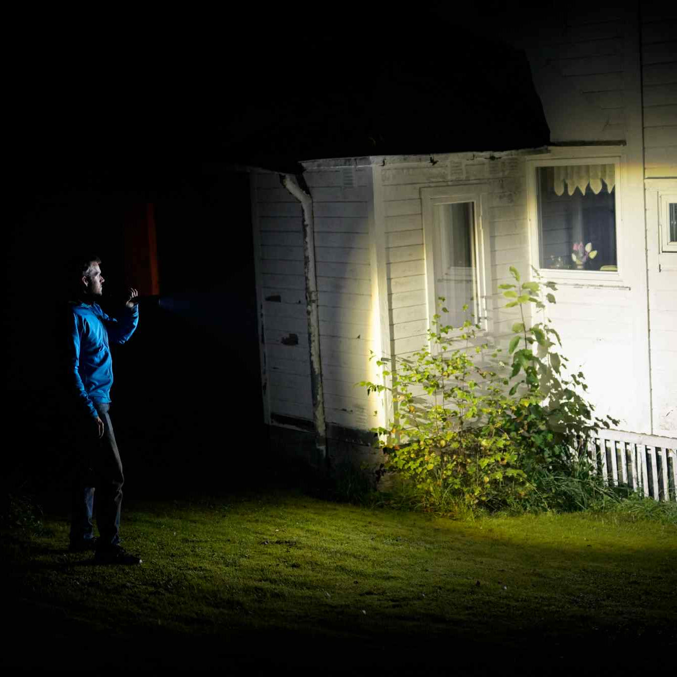 Person holding a flashlight outside a house at night