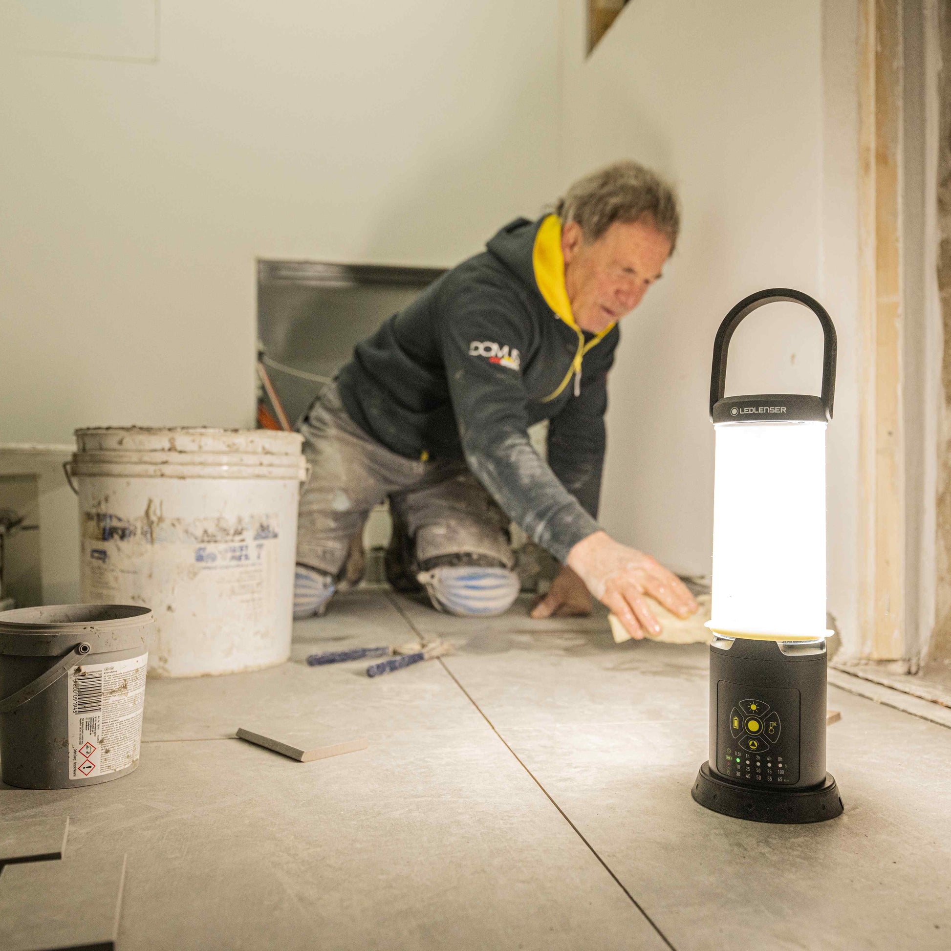 Person working on a floor installation project with a portable light illuminating the area.