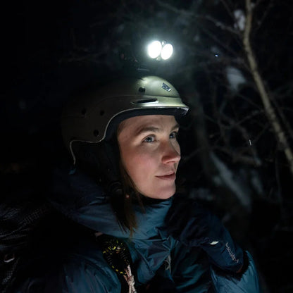 Person wearing a helmet with a light source in a dark forest setting