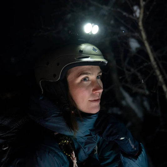 Person wearing a helmet with a light source in a dark forest setting