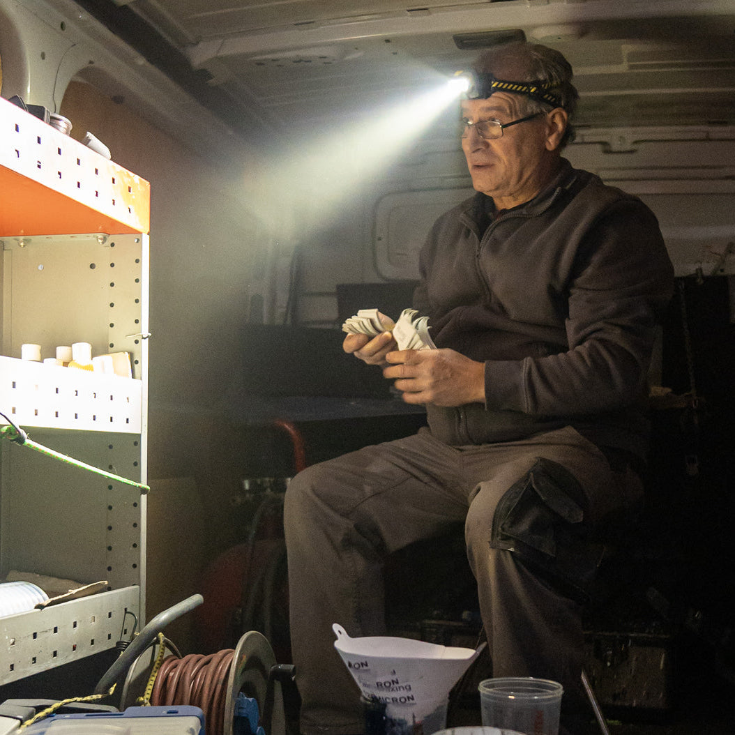 Man sitting inside a vehicle with a light shining on him, surrounded by tools and equipment.