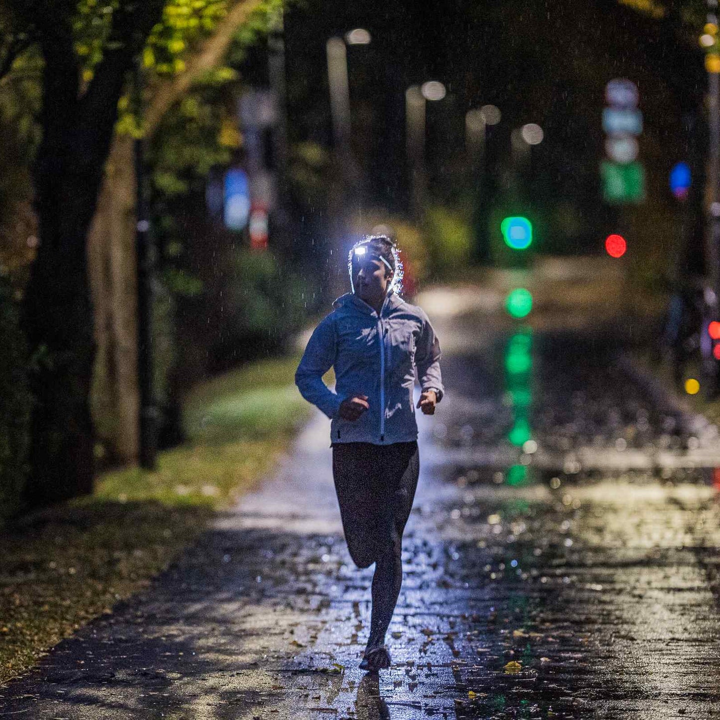 Person running on a dark, rain-soaked street at night with a headlamp.