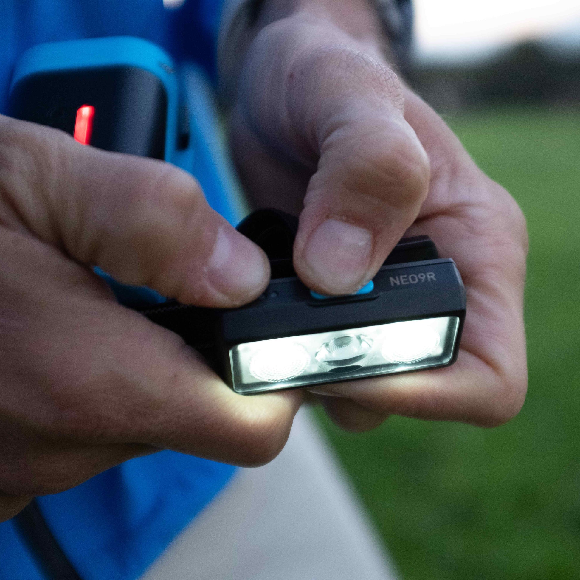 Person holding a small electronic device with a blurred green field in the background